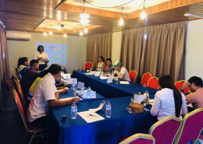 A group of people sitting at tables in front of blue cloth.